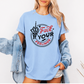 A woman wearing an oversized light blue graphic T-shirt with a circular design that reads 'Fuck Your Feelings' in black and red, styled with a light wash denim jacket draped off the shoulders against a plain white background. Purchase from Coffee and Moo NZ.