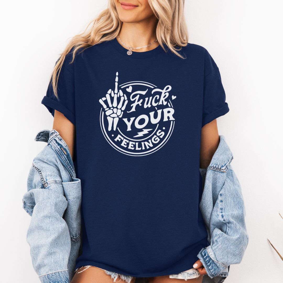 A woman wearing an oversized navy blue graphic t-shirt with a white circular design featuring a hand gesture and the text 'Fuck YOUR FEELINGS'. She has a light-wash denim jacket draped off her shoulders and is standing against a plain white wall. Purchase from Coffee and Moo NZ.
