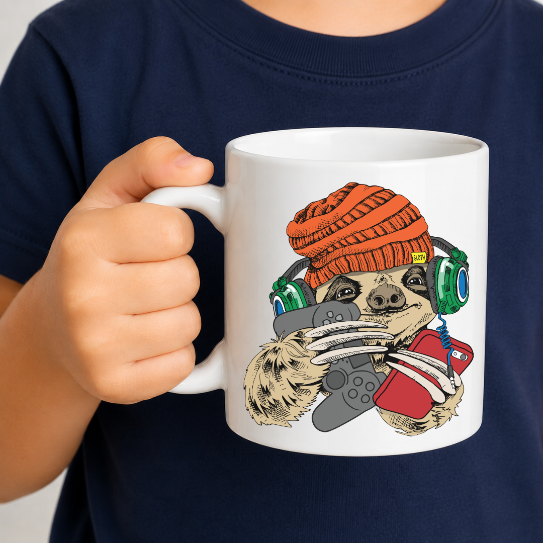 A child holding a white ceramic mug with a cartoon graphic of a sloth wearing an orange beanie, green headphones, and a red shirt while holding a game controller. Grab your gaming sloth mug from Coffee and Moo NZ.