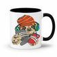 A white ceramic mug with a black interior and handle, featuring a cartoon sloth graphic wearing an orange knit beanie, green headphones, and holding a red phone and gray game controller. Grab your gaming sloth mug from Coffee and Moo NZ.