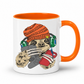 A white ceramic mug with a bright orange handle and interior, featuring a cartoon sloth wearing an orange knit beanie, green headphones, and holding a grey game controller and a red smartphone. Grab your gaming sloth mug from Coffee and Moo NZ.