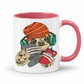A white ceramic mug with a pink interior and handle, featuring a cartoon sloth wearing an orange knit beanie, green headphones, and holding a red phone and grey game controller. Grab your gaming sloth mug from Coffee and Moo NZ.