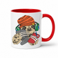 A white ceramic mug with a red interior and red handle, featuring a cartoon sloth wearing an orange knit beanie, green headphones, and holding a grey game controller and red drink. Grab your gaming sloth mug from Coffee and Moo NZ.