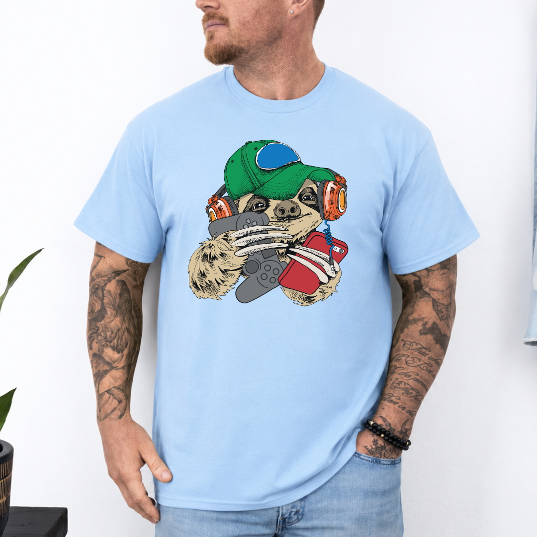 A man wearing a baby blue t-shirt with a cartoon sloth graphic wearing a cap, oversized headphones, while holding a grey gaming controller and red phone, set against a white wall background. Grab your tee from Coffee and Moo NZ.