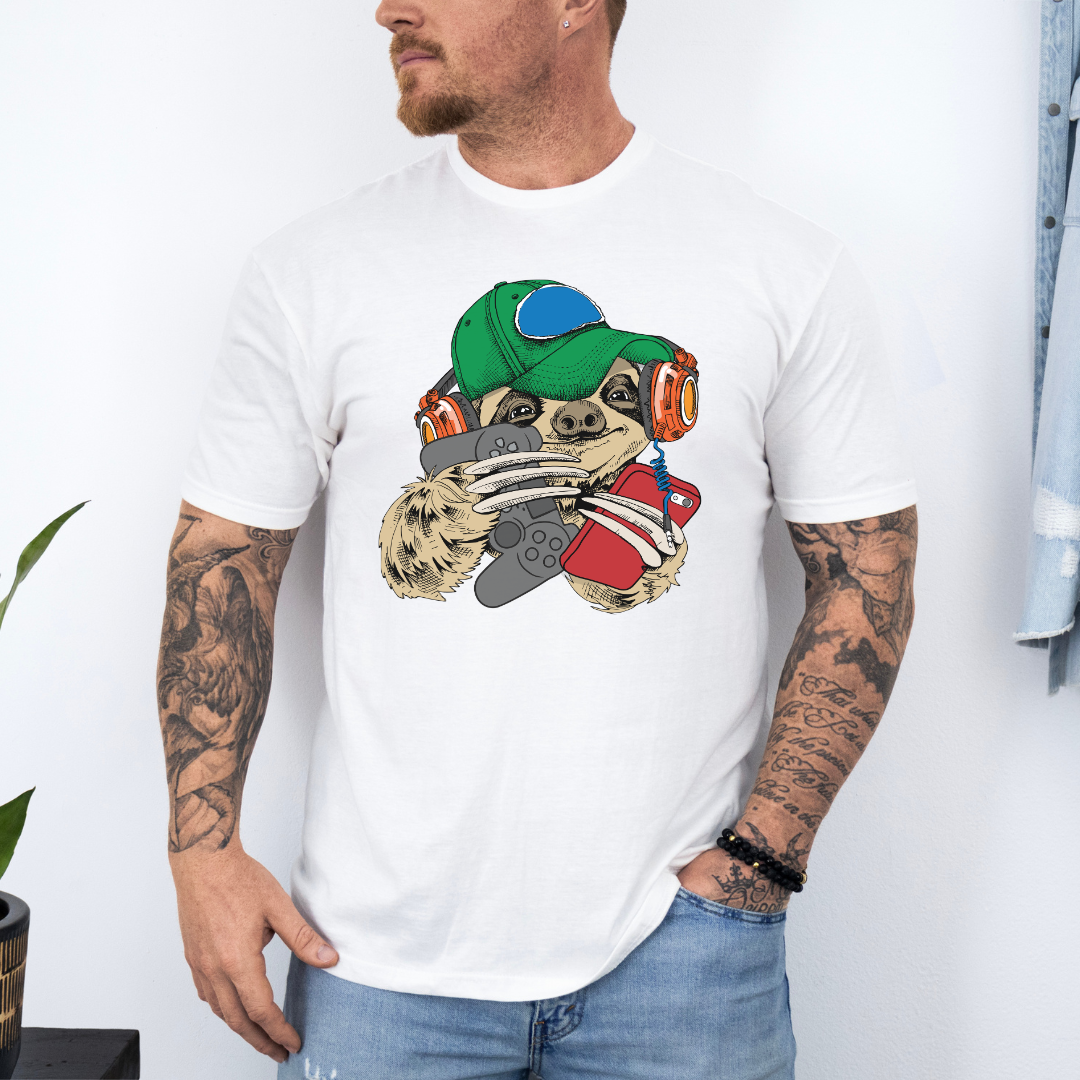 A man wearing a white t-shirt with a cartoon sloth graphic wearing a cap, oversized headphones, while holding a grey gaming controller and red phone, set against a white wall background. Grab your tee from Coffee and Moo NZ.