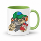 A white ceramic mug with a light green interior and handle, featuring a cartoon sloth wearing a green cap, orange headphones, and holding a grey game controller and a red phone. Purchase your mug from Coffee and Moo NZ.