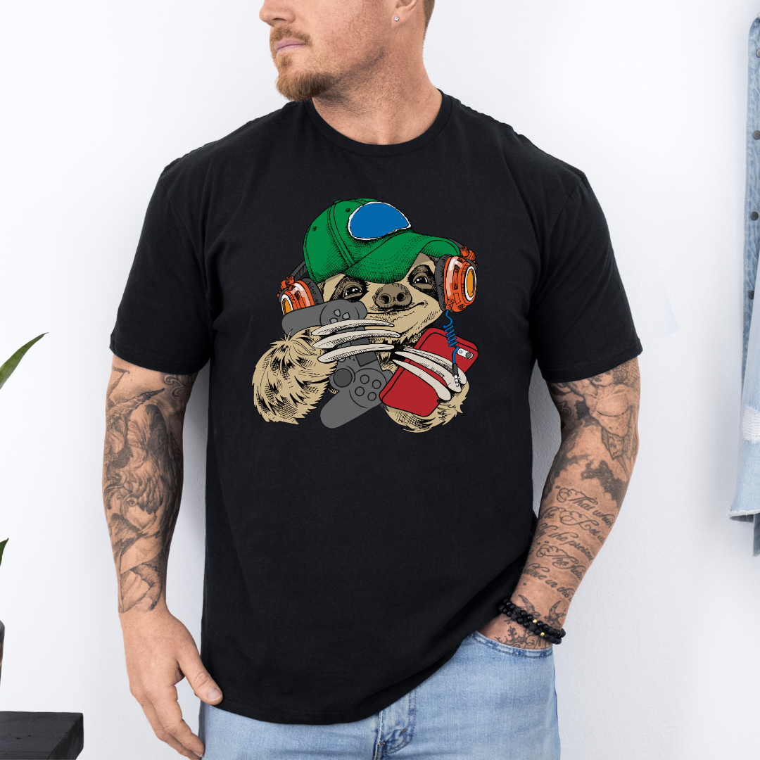 A man wearing a black t-shirt with a cartoon sloth graphic wearing a cap, oversized headphones, while holding a grey gaming controller and red phone, set against a white wall background. Grab your tee from Coffee and Moo NZ.