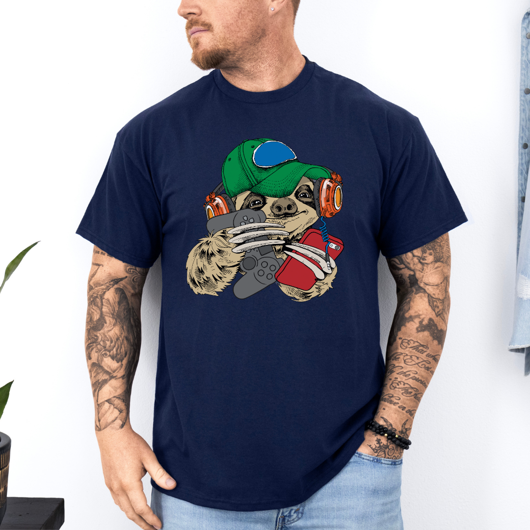 A man wearing a navy blue t-shirt with a cartoon sloth graphic wearing a cap, oversized headphones, while holding a grey gaming controller and red phone, set against a white wall background. Grab your tee from Coffee and Moo NZ.