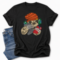 A black short-sleeve graphic T-shirt laid flat on a white background, styled with folded blue jeans at the lower left. The shirt features a colorful cartoon sloth wearing an orange knit beanie, green headphones, and holding a red phone and grey controller. Grab your tee from Coffee and Moo NZ.
