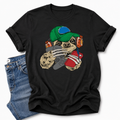 A black short-sleeve t-shirt with a colorful graphic of a sloth wearing a green cap, orange headphones, while holding a grey controller and red phone. The shirt is styled flat-lay with a pair of blue jeans on a light gray background. Grab your tee from Coffee and Moo NZ.