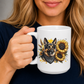 A woman holding a white ceramic mug with a detailed graphic of a German Shepherd wearing a bandana, surrounded by sunflowers and wheat. The woman is wearing a navy blue shirt, and the background is a soft, neutral grey. Grab your mug from Coffee and Moo NZ.