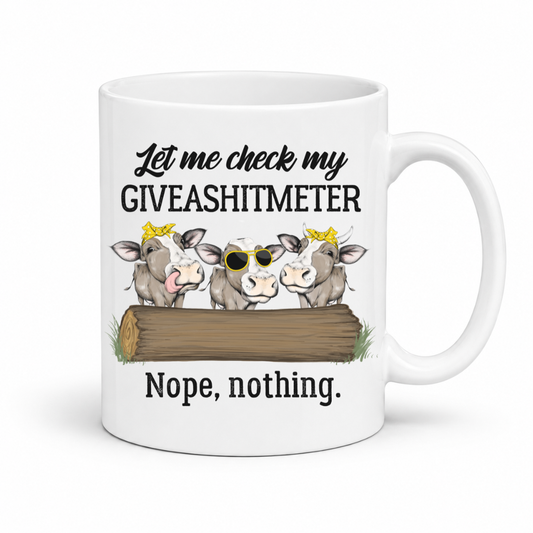 A white ceramic mug with a humorous graphic that reads 'Let me check my GIVEASHITMETER' above three cartoon cows peeking over a log, and 'Nope, nothing.' below, shown on a plain white background. Grab your cheeky mug from Coffee and Moo NZ.