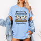 A woman wearing a light blue graphic t-shirt with a cow design and the text 'Let me check my GIVEASHITMETER Nope, nothing.' She has a light blue denim jacket off her shoulders against a plain white background. Grab your from Coffee and Moo NZ.