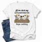 A white graphic t-shirt featuring a cartoon design of three cows and the text 'Let me check my GIVEASHITMETER Nope, nothing.' styled flat-lay next to a pair of blue jeans on a white background. Grab your from Coffee and Moo NZ.