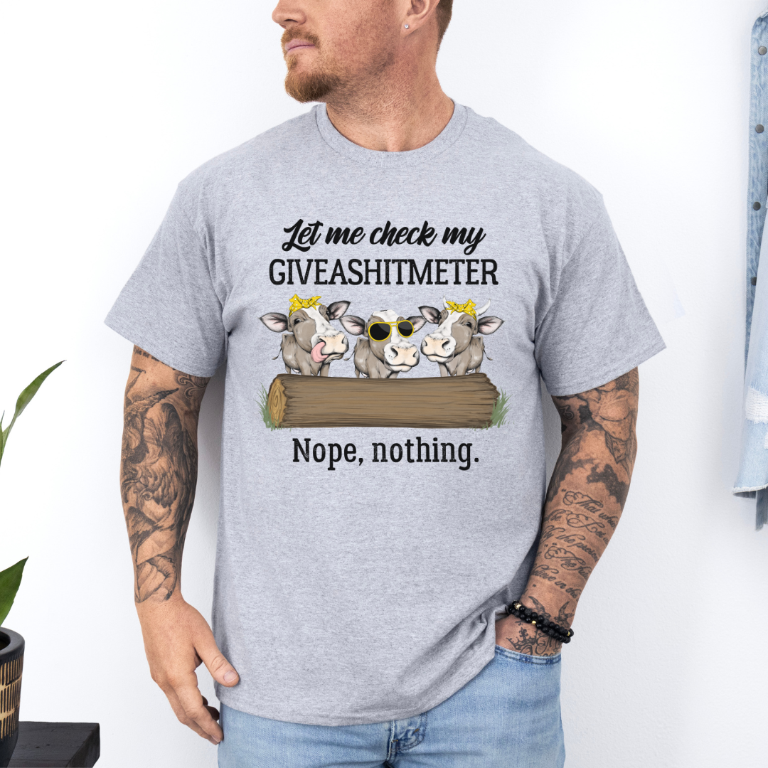 A man wearing a light heather gray graphic t-shirt with a humorous text and cow illustration, paired with blue jeans in a bright indoor setting. Grab your from Coffee and Moo NZ.