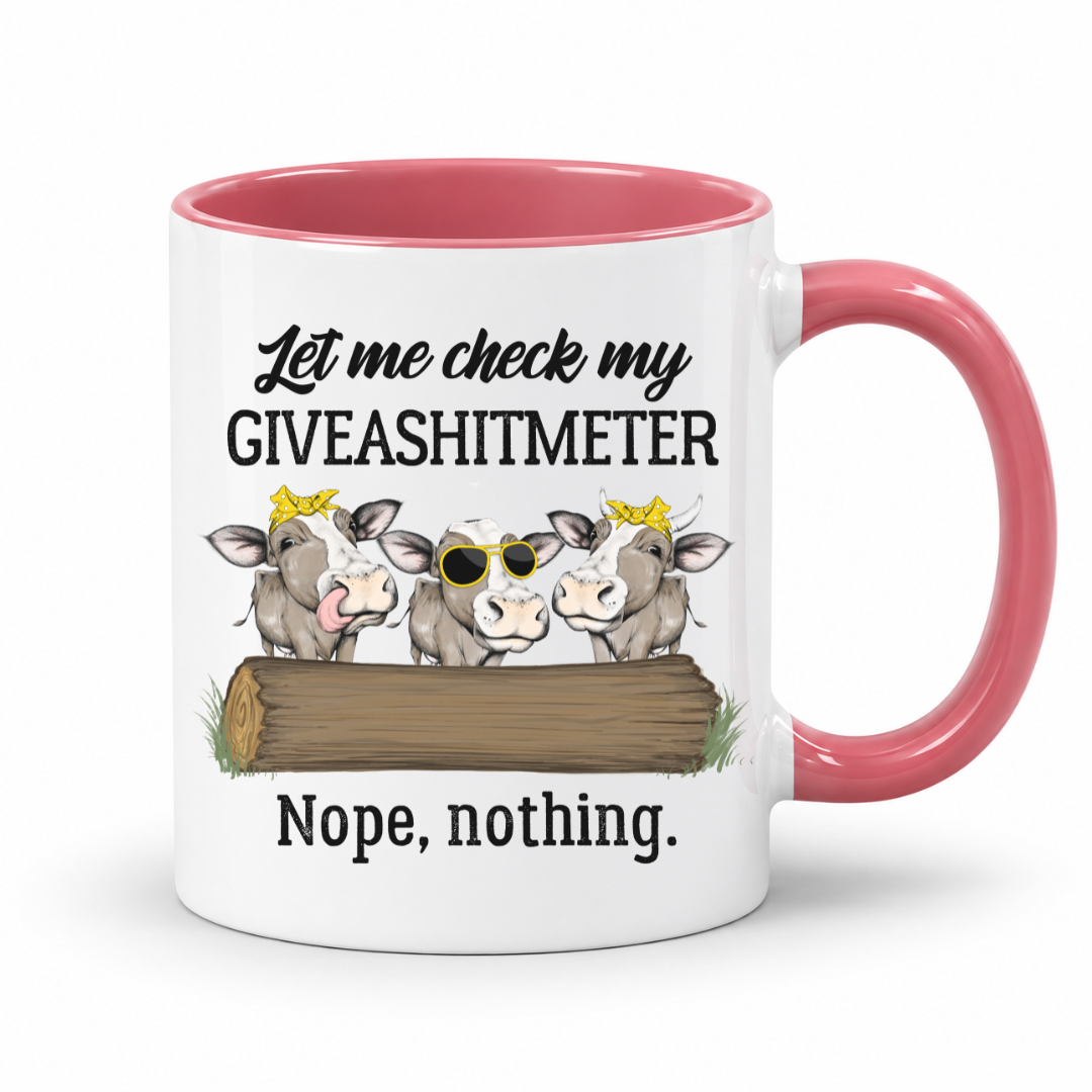 A white ceramic mug with a pink interior and handle, featuring a humorous graphic of three cartoon cows behind a log with the text 'Let me check my GIVEASHITMETER' and 'Nope, nothing.'. Grab your cheeky mug from Coffee and Moo NZ.