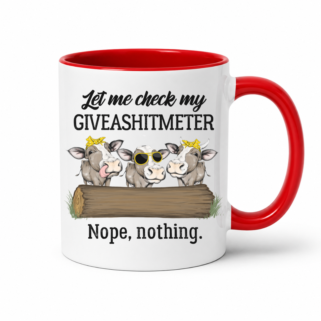 A white ceramic mug with a red interior and red handle, featuring a humorous graphic of three cartoon cows peeking over a log with the text 'Let me check my GIVEASHITMETER Nope, nothing.' on a clean white background. Grab your cheeky mug from Coffee and Moo NZ.