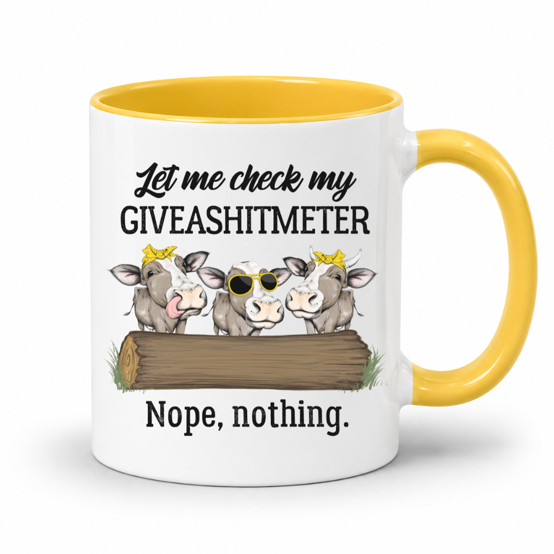 A white ceramic mug with a yellow interior and yellow handle, featuring a cartoon illustration of three cows behind a log with the text 'Let me check my GIVEASHITMETER' above and 'Nope, nothing.' below. Grab your cheeky mug from Coffee and Moo NZ.