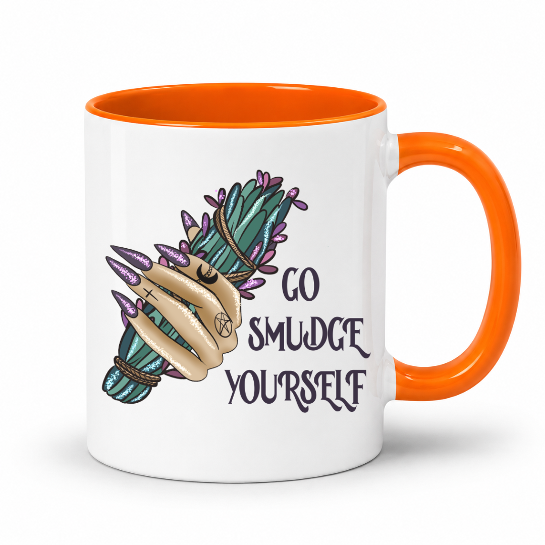 A white ceramic mug with a bright orange handle and interior, featuring a graphic of a tattooed hand holding a green and purple smudge stick bundle next to the text 'GO SMUDGE YOURSELF' in dark lettering. Purchase from Coffee and Moo NZ.