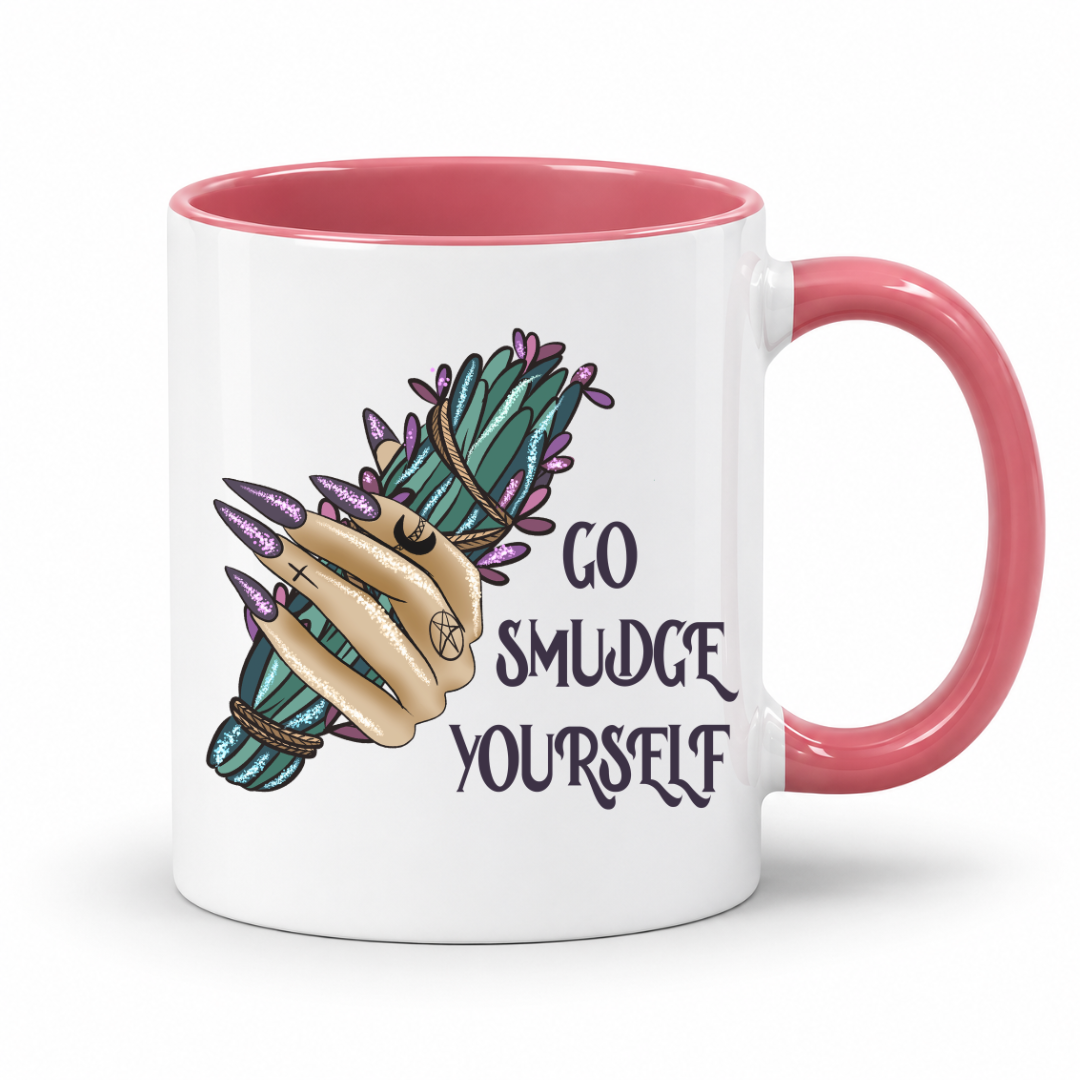 A white ceramic mug with a pink interior and handle, featuring a graphic of a hand with long purple nails holding a green and purple smudge stick bundle, next to the text 'GO SMUDGE YOURSELF'. Purchase from Coffee and Moo NZ.