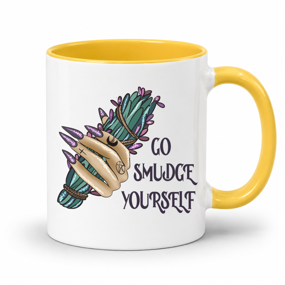 A white ceramic coffee mug with a yellow interior and handle, featuring a graphic of a hand with long nails holding a smudge sticks bundle next to the text 'GO SMUDGE YOURSELF'. Purchase from Coffee and Moo NZ.