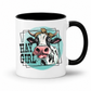 A white ceramic coffee mug with a black interior and black handle, featuring a graphic of a cow with a leopard-print headband and the text 'HAY GIRL' on a light teal oval background.  from Coffee and Moo NZ.