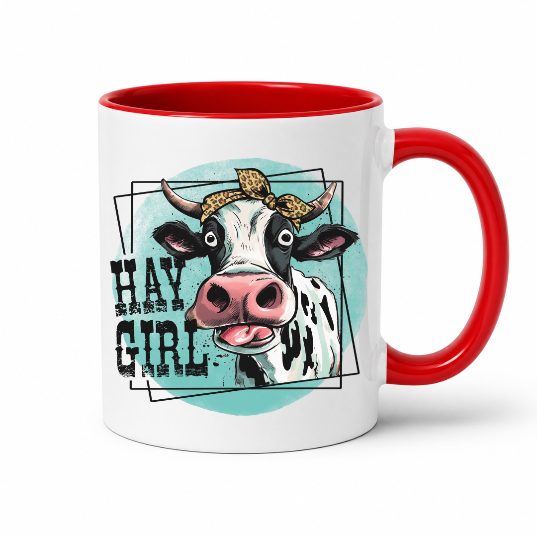 A white ceramic coffee mug with a red interior and red handle, featuring a graphic of a cow with the text 'HAY GIRL' on the front.  from Coffee and Moo NZ.
