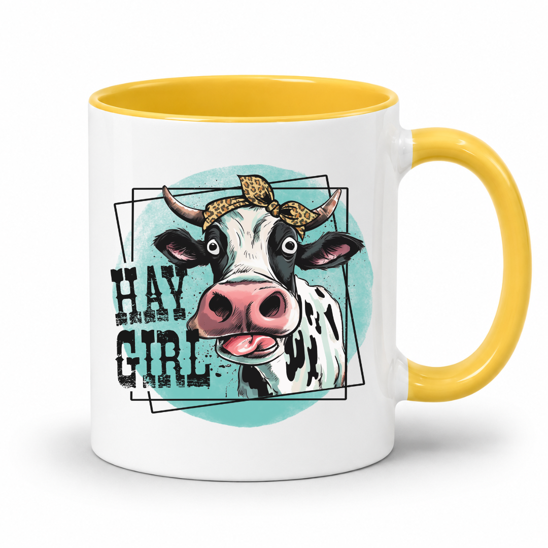 A white ceramic coffee mug with a yellow interior and handle, featuring a graphic illustration of a cow wearing a leopard-print bandana and the text 'HAY GIRL' on a light teal circular background.  from Coffee and Moo NZ.
