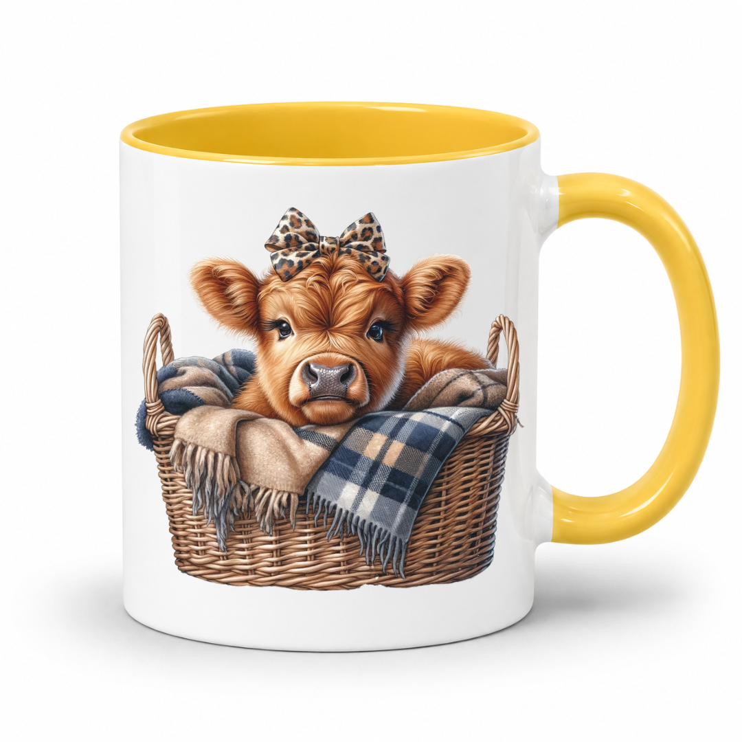 A white ceramic mug with a yellow interior and handle, featuring a printed illustration of a brown calf in a wicker basket with a plaid blanket and leopard-print bow. from Coffee and Moo NZ.
