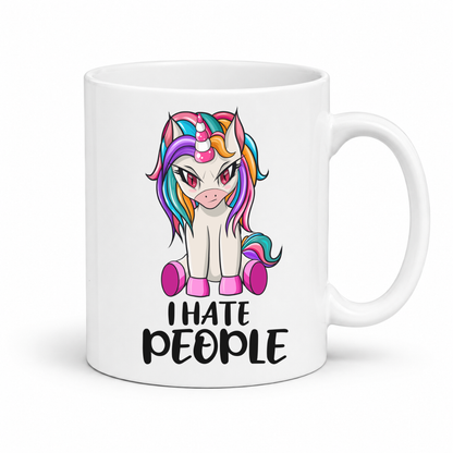 A white ceramic mug featuring a cartoon illustration of a white unicorn with a vibrant rainbow mane and tail, sitting above the text 'I HATE PEOPLE' in black. The mug is shown on a clean white background with a soft shadow. From Coffee and Moo NZ.