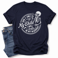 A navy blue short-sleeve t-shirt with a white graphic print of a skeleton and the text 'When it comes to My Child I Will Smile in my mugshot', styled flat-lay next to a pair of blue jeans on a white background. Grab your tee from Coffee and Moo NZ.