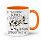 A white ceramic coffee mug with a bright orange handle and interior, featuring a cartoon cow and the humorous text 'IF SWEARING BURNED CALORIES I'D BE ONE SKINNY HEIFER' printed on the front. purchase from Coffee and Moo NZ.