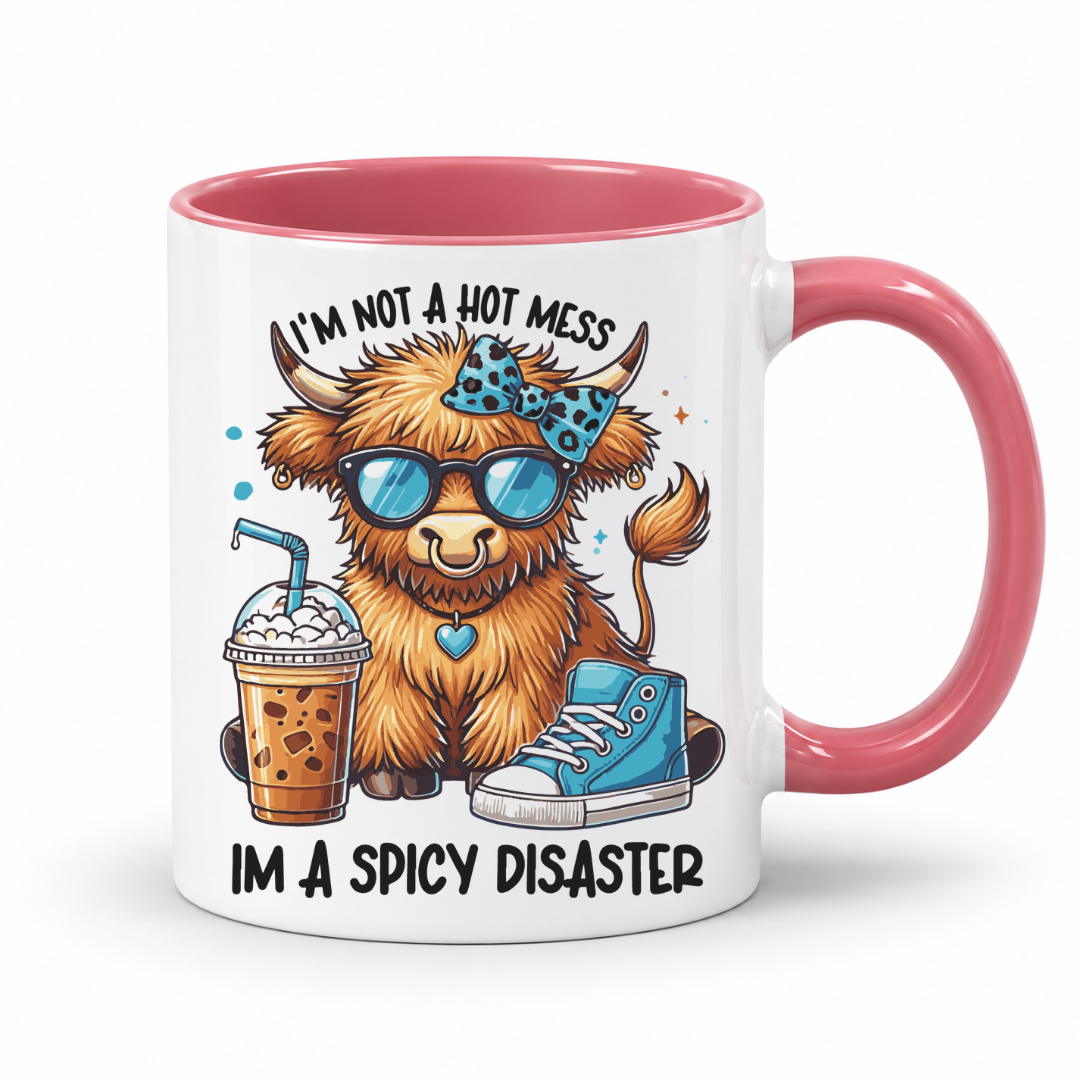 A white ceramic mug with a pink interior and handle, featuring a cartoon Highland cow wearing blue sunglasses and a blue bow tie, next to an iced coffee and a blue sneaker. The text reads 'I'M NOT A HOT MESS IM A SPICY DISASTER'. from Coffee and Moo NZ.
