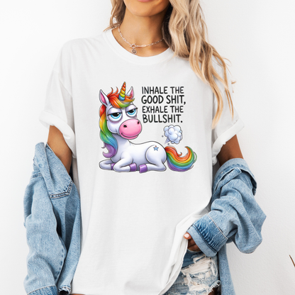 A woman wearing a white graphic t-shirt with a cartoon rainbow unicorn and the text 'INHALE THE GOOD SHIT, EXHALE THE BULLSHIT.' She has a light blue denim jacket draped off her shoulders and is wearing distressed jeans against a plain white background.  Purchase from Coffee and Moo NZ.