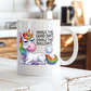 A white ceramic coffee mug with a cartoon rainbow unicorn and the text 'INHALE THE GOOD SHIT, EXHALE THE BULLSHIT.' shown on a rustic white wooden table with a blurred kitchen background. Purchase from Coffee and Moo NZ.