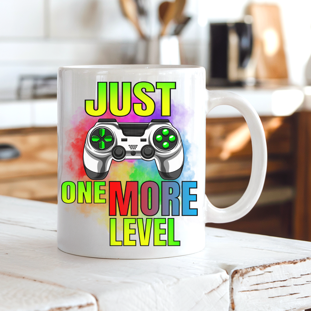 Just One More Level gaming coffee mug on a country kitchen bench, featuring a colourful gaming controller and rainbow design, by Coffee and Moo.