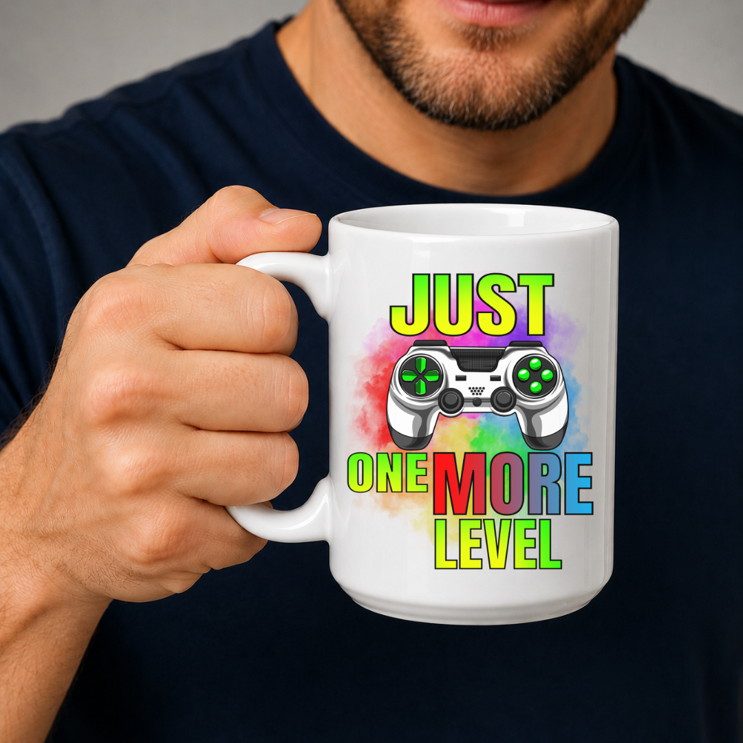 Male holding Just One More Level gaming coffee mug, showcasing the colourful gaming controller and bold lettering, by Coffee and Moo.