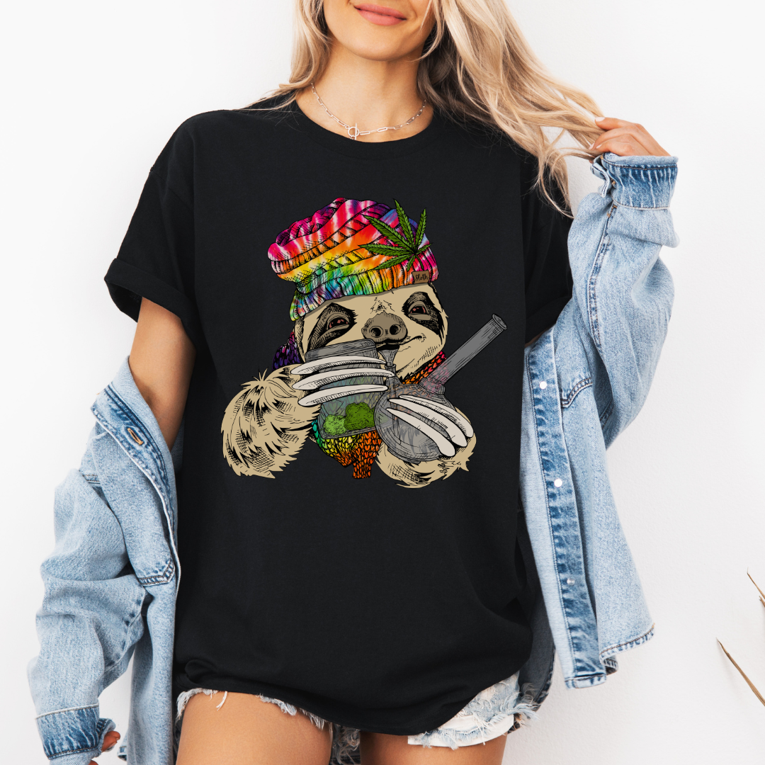 A woman wearing a black unhinged adult graphic tee features our resident zen master—a delightfully baked sloth rocking a vibrant, colourful tie-dye beanie topped with a cannabis leaf, proudly clutching a bong and a jar of premium green buds. Grab your sloth stoner tee from Coffee and Moo NZ.