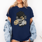 A woman wearing a navy blue short-sleeve graphic t-shirt with a stylized Emo sloth wearing a beanie, headphones, and holding a coffee cup with the word "TEARS" on it. Grab your tee from Coffee and Moo NZ.
