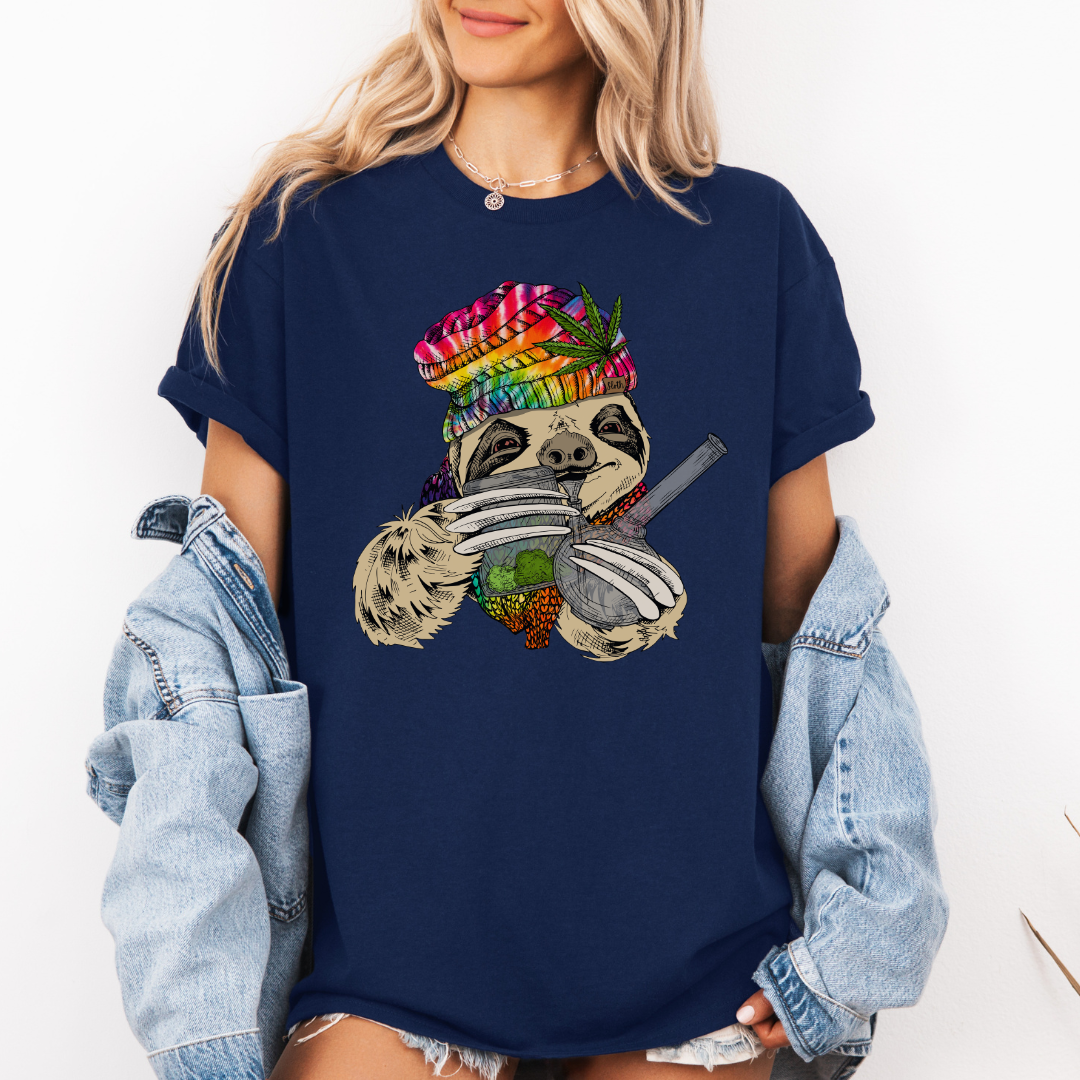 A woman wearing a navy unhinged adult graphic tee features our resident zen master—a delightfully baked sloth rocking a vibrant, colourful tie-dye beanie topped with a cannabis leaf, proudly clutching a bong and a jar of premium green buds. Grab your sloth stoner tee from Coffee and Moo NZ.