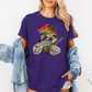 A woman wearing a purple unhinged adult graphic tee features our resident zen master—a delightfully baked sloth rocking a vibrant, colourful tie-dye beanie topped with a cannabis leaf, proudly clutching a bong and a jar of premium green buds. Grab your sloth stoner tee from Coffee and Moo NZ.