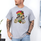 A man wearing a grey unhinged adult graphic tee features our resident zen master—a delightfully baked sloth rocking a vibrant, colourful tie-dye beanie topped with a cannabis leaf, proudly clutching a bong and a jar of premium green buds. Grab your sloth stoner tee from Coffee and Moo NZ.