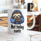 A white ceramic coffee mug with a cartoon sloth wearing a blue hoodie and the text 'Not today cunts' printed on it, sitting on a rustic white wooden table with a blurred kitchen background.  from Coffee and Moo.
