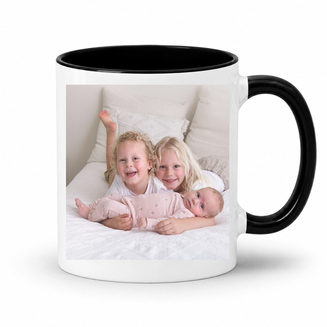 A white ceramic mug with a black interior and black handle, featuring a printed custom photo of three children on the front, set against a plain white background. Grab your custom photo mug from Coffee and Moo NZ.