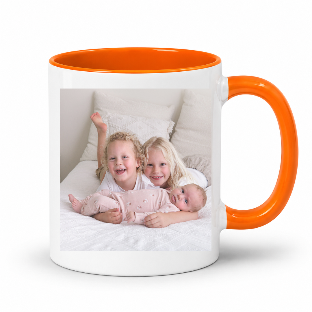 A white ceramic mug with a bright orange handle and interior, featuring a printed custom photo of three children on the front, set against a plain white background. Grab your custom photo mug from Coffee and Moo NZ.
