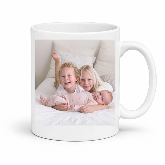 A white ceramic mug with a custom printed photo of three children in a photoshoot, shown against a plain white background. Grab your custom photo mug from Coffee and Moo
