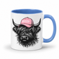 A white ceramic mug with a blue interior and handle, featuring a graphic of a shaggy Highland cow wearing a pink cap with the word 'BOSSY' in white text. grab your bossy  mug from Coffee and Moo NZ.
