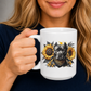 A woman holding a white ceramic mug with a graphic of a black pitbull-dog surrounded by yellow sunflowers. wearing a navy blue shirt. Grab your mug from Coffee and Moo NZ.
