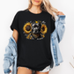 A woman wearing a black graphic t-shirt with a printed design of a dark coloured pitbull dog wearing a black and gold bandana, surrounded by yellow sunflowers. Grab your tee from Coffee and Moo NZ.
