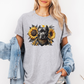 A woman wearing a grey graphic t-shirt with a printed design of a dark coloured pitbull dog wearing a black and gold bandana, surrounded by yellow sunflowers. Grab your tee from Coffee and Moo NZ.